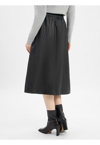 Jupe noire mi-longue avec une taille élastique, confectionnée dans un matériau lisse. Associée à des bottes à talons hauts noires.