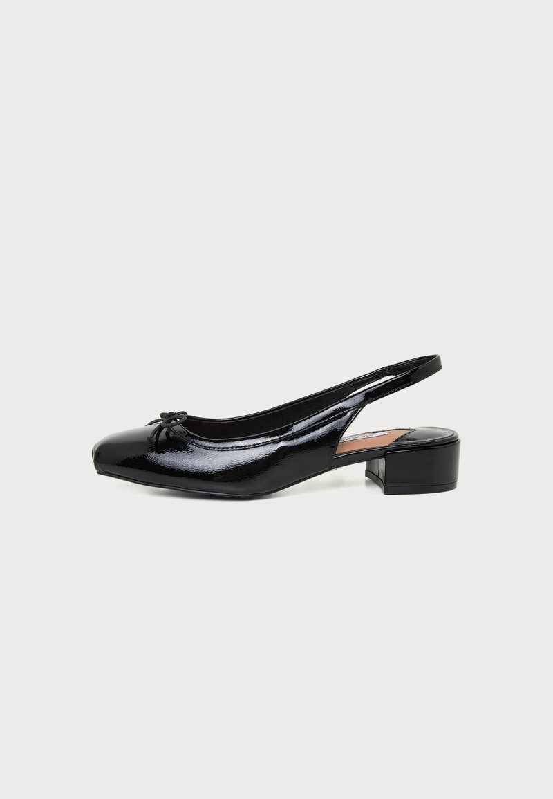 Μαύρο παπούτσι slingback από δερμάτινο βερνίκι με χαμηλό τετράγωνο τακούνι και μικρό φιόγκο στο στρογγυλεμένο μπροστινό μέρος, απεικονίζεται σε πλάγια όψη σε λευκό φόντο.