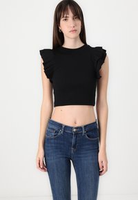 Black cropped top with ruffled sleeves, paired with fitted blue denim jeans. Clean lines and smooth texture, focusing on minimalist design.