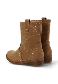 Botas de tobillo de ante marrón con costuras decorativas y tachuelas metálicas, que presentan un diseño curvado y un tacón bajo apilado.