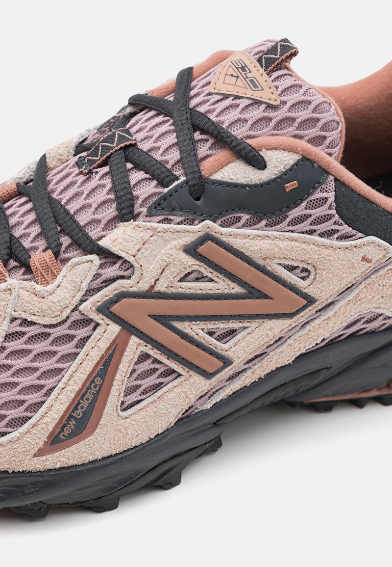Chaussures de trail running avec une tige en mesh respirant de couleur rose clair, accents noirs, superpositions en daim texturé et semelle extérieure noire robuste.