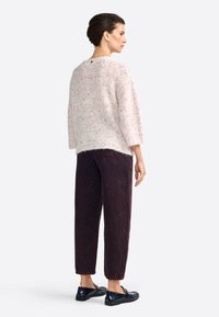 Maglione a maglia rosa chiaro con spruzzi, abbinato a pantaloni a gamba stretta di un borgogna scuro. Scarpe slip-on nere. Vista mostra il retro dell'outfit.