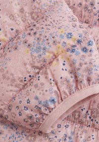 Vadderad jacka i ljusrosa med ett blommönster i blått, gult och lila. Har elastiska ärmslut och en mjuk textur.