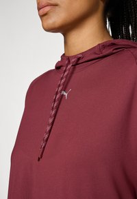 En vinröd hoodie med dragsko på huvan, med en silverfärgad logotyp på bröstet och en strukturerad dragsko. Mjuk, slät tyg med en figurnära passform.