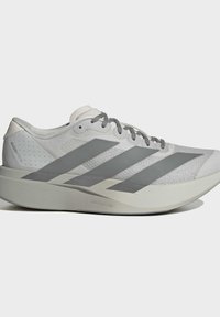 Ανοιχτό γκρι αθλητικό παπούτσι Adidas με σκούρες γκρι ρίγες, επενδυμένη σόλα, πλέγμα ανώτερο μέρος και κλείσιμο με κορδόνια, απεικονίζεται από το πλάι σε απλό φόντο.