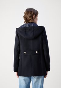 Jūrinės vilnos paltas su gobtuvu, turintis lygią pamušalą, dvigubo užsegimo sidabro mygtukus ir tekstūruotą medžiagą.