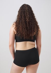 Svart bomullsbalkong och shorts med en sömlös design och ett mjukt elastiskt midjeband, sedd bakifrån. Lockigt hår döljer utsikten.