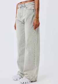 Jeans de pierna ancha en gris claro con un diseño clásico de cinco bolsillos, hechos de mezclilla. Presenta un cierre de botón y una textura desgastada.