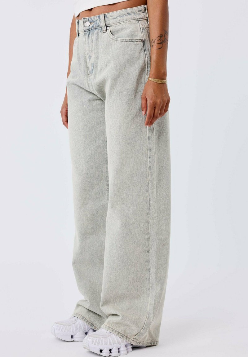 Jeans de pierna ancha en gris claro con un diseño clásico de cinco bolsillos, hechos de mezclilla. Presenta un cierre de botón y una textura desgastada.