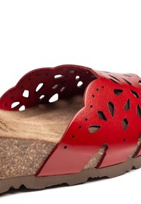 Red leather slide sandal featuring cut-out floral design, curved upper edge, and cork footbed with textured surface. Rubber sole for traction.