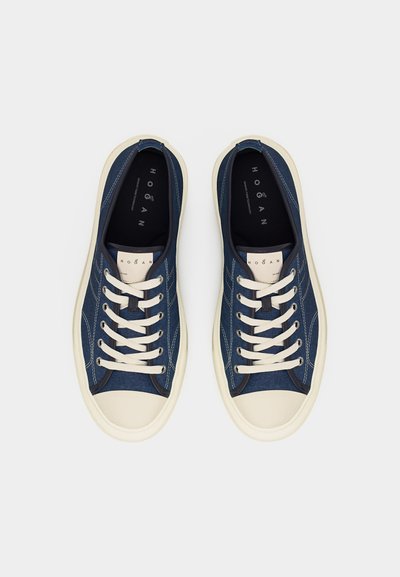 Ζευγάρι ναυτικά μπλε πάνινα αθλητικά παπούτσια με λευκά κορδόνια και σόλες, σε θέα από πάνω πάνω σε απλό γκρι φόντο.