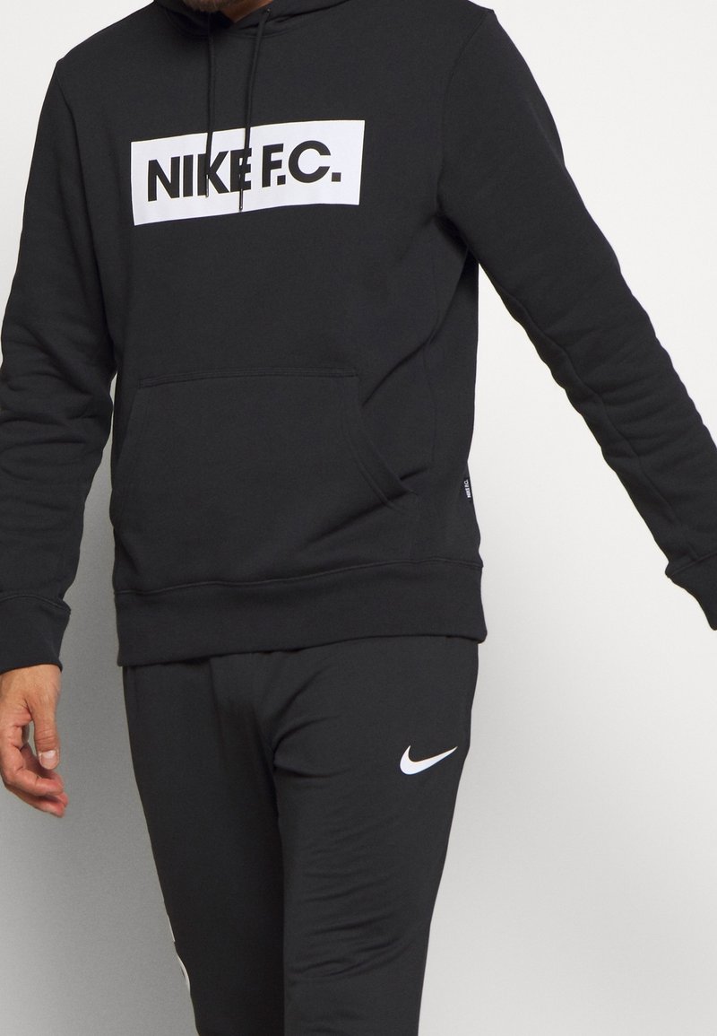 Sweat à capuche noir avec logo Nike F.C. blanc, poche kangourou, poignets et ourlet côtelés. Associé à un pantalon de jogging noir assorti.