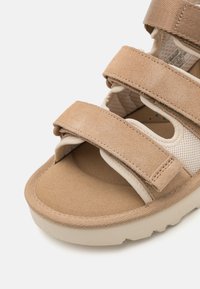 Beige semsket sandal med tre justerbare borrelås, polstret innersåle og teksturert gummisåle for bedre grep og komfort.