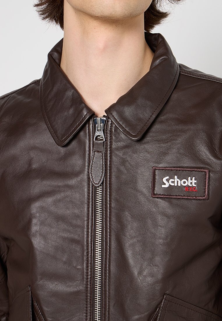 Veste en cuir marron avec fermeture éclair à l'avant, col pointu et patch logo Schott N.Y.C. sur la poitrine gauche. Texture lisse avec un éclat noticeable.