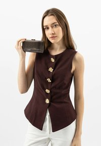 Burgundowa bluzka bez rękawów z złotymi guzikami w kształcie kwiatu, zestawiona z brązową torebką wężową z materiału syntetycznego. Teksturowany materiał i wyrafinowana sylwetka.