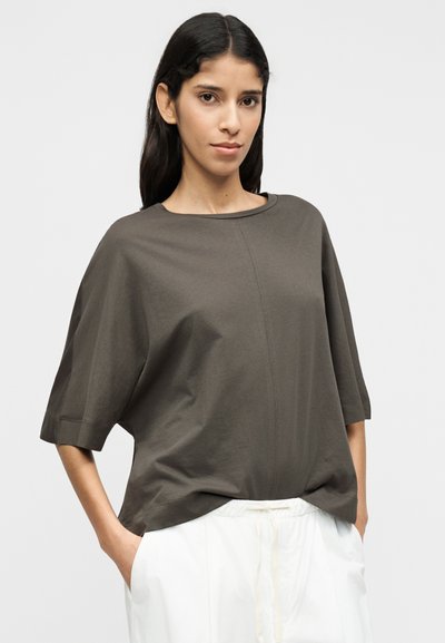 Γκρι άνετη μπλούζα με κοντά μανίκια και στρογγυλή λαιμόκοψη. Κατασκευασμένη από απαλό ύφασμα, με ελαφρώς καμπυλωτό τελείωμα και ελάχιστες ραφές.