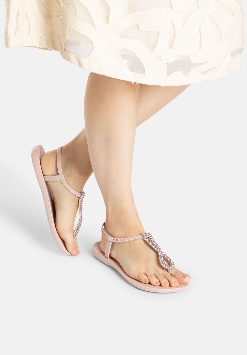 Rosa flache Sandalen mit einem T-Riemen-Design, strukturiert mit Perlenakzenten und einer glatten Sohle. Die Riemen bestehen aus flexiblem Material.