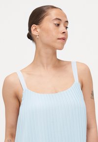 Light blue pleated dress with thin straps, featuring a square neckline and textured fabric. Simple design without additional embellishments.