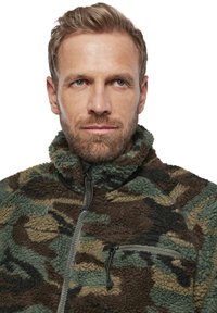Pruun ja roheline kamuflaaž fleecetagi kõrge kraega, poolsiidise eest ning tõmbluku taskuga rinnal. Pehme tekstuur ja juhuslik disain.