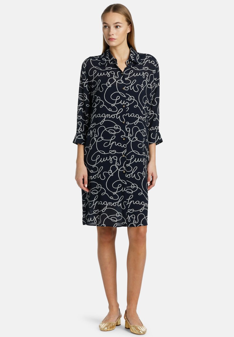 Rochie bleumarin cu model de text cursiv alb, mâneci lungi, guler și detalii cu nasturi; design de lungime până la genunchi; material ușor.