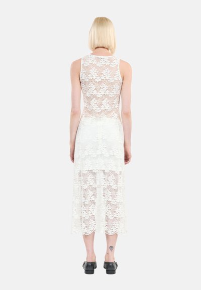 Robes en dentelle blanche avec un design sans manches, présentant une texture en couches et un ourlet festonné. Le tissu affiche des motifs floraux.