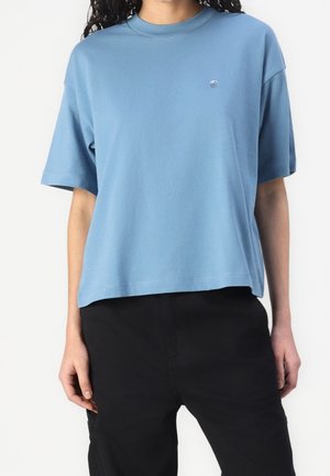 Jasnoniebieska, krótka koszulka z miękkiej bawełny z okrągłym dekoltem i małym logo na piersi, zestawiona z czarnymi spodniami.