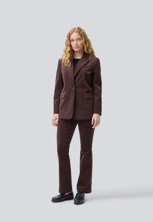 Un costume en velours côtelé brun avec un blazer ajusté et un pantalon évasé. Les deux pièces présentent une texture douce, une fermeture à un bouton et des poches avant.