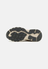 Sneaker-Außensohle mit schwarzem Gummi-Profil und tiefen Rillen und Mustern, kontrastiert durch eine beigen Zwischensohle für verbesserten Halt und Unterstützung.