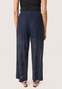 Marineblauwe flared broek van kant met geometrische uitsneden en een haakpatroon. Beschikt over een comfortabele elastische tailleband.