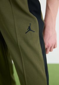 Olivgrön och svarta sportbyxor med texturerat tyg, med en svart Jumpman-logotyp på sidan och en figurnära design.