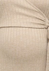 Tissu beige côtelé avec des rayures verticales et une légère texture, présentant un détail froncé sur un côté pour plus de finition.