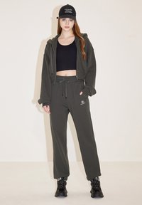 Dunkelgrüner, cropped Hoodie und passende Jogginghose aus weichem Stoff, kombiniert mit einer schwarzen Kappe mit weißem Text und schwarzen Sneakers.