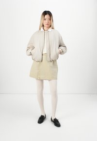 Beige bomber bunda, bílý top s límečkem, světle zelená kordovská sukně, bílé punčocháče a černé boty. Jednoduchý design s volným střihem.