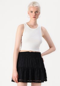Hvit ribbet crop-top kombinert med et svart blondekjole med flere lag og en smocket midje. Glatt tekstur med lagdelte designdetaljer.