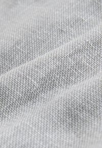 Tissu gris clair avec une texture fine et serrée en maille et des plis doux et subtils créant de douces ondulations à la surface.