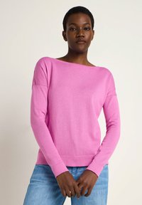 Rosa Strickpullover mit Rundhalsausschnitt und langen Ärmeln, mit einem gerippten Saum. Getragen mit hellblauen Jeans. Glatte Textur.
