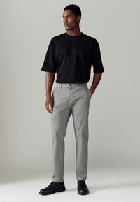 T-shirt noir à manches courtes associé à un pantalon gris clair. Le pantalon présente une coupe droite et l'ensemble est complété par des chaussures noires.
