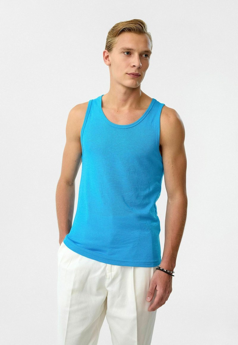 Blauwe tanktop van zachte stof, met een ronde halslijn en mouwloos ontwerp, gecombineerd met een witte broek. Minimalistische stijl.
