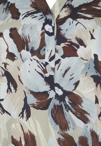 Bloes met bloemenprint, bestaande uit grote lichtblauwe, bruine en crèmekleurige bloemen op een zachte stof. Het ontwerp heeft een v-hals en een subtiele textuur.