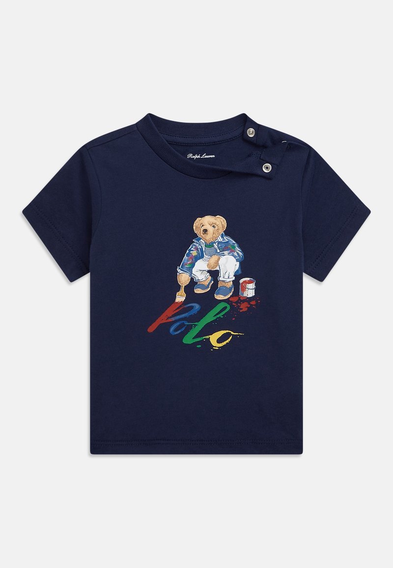Námořnická modrá bavlněná tričko s ilustrací medvěda a barevným textem "Polo" pod ním. Dvě patentky na rameni pro snadné oblékání.