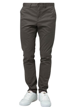 Pantalones ajustados de color gris oscuro combinados con zapatillas blancas bajas en una persona de pie contra un fondo blanco.