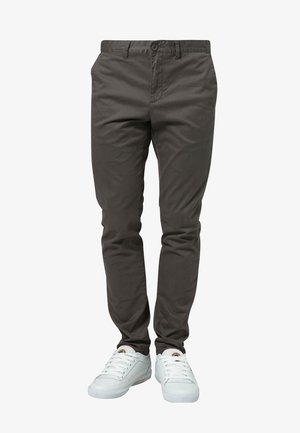 Donkergrijze slim-fit broek gecombineerd met witte lage sneakers op een persoon die tegen een witte achtergrond staat.