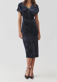Robe en velours bleu marine avec une silhouette ajustée, des manches courtes en dolman et un décolleté en V profond. Longueur midi, texture douce et finition lisse.