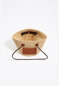 Bolso de cubo de paja trenzada con base de cuero marrón claro y asas de cordón marrón oscuro. Presenta una etiqueta de cuero con marca y un acabado texturizado.
