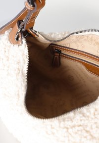 Weiße, flauschige Handtasche mit strukturiertem Außenmaterial und einem glatten Ledertragegurt. Das Innere verfügt über eine Reißverschlusstasche und ein markiertes Innenfutter. Reißverschlussverschluss.