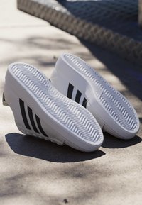 Paar weiße Sneakers mit schwarzen Streifen, die mit der Sohle nach oben auf einer Betonoberfläche im Freien liegen, mit Schatten.