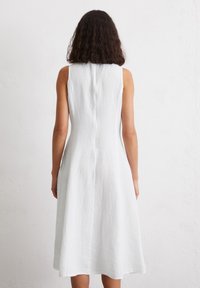 Sleeveless, white linen dress with a fitted bodice and a flared A-line skirt, featuring a central back seam and a smooth texture.