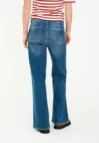 Blauwe denim jeans met een ontspannen pasvorm, brede pijpen en twee achterzakken. De stof heeft een gladde textuur met subtiele vervaging.