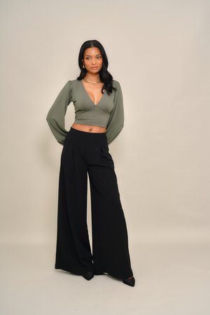 Ελιάς πράσινο crop top με μακριά μανίκια, βαθύ V-λαιμόκοψη· συνδυασμένο με ψηλόμεσο, μαύρο παντελόνι φαρδύ στα πόδια· απαλό ύφασμα, μινιμαλιστικός σχεδιασμός.