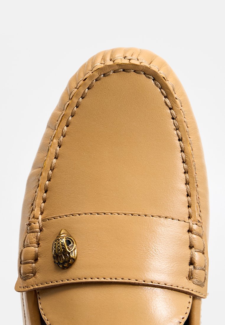 Mocassin en cuir tan avec des coutures détaillées et un petit ornement en laiton en forme de hibou sur le devant.